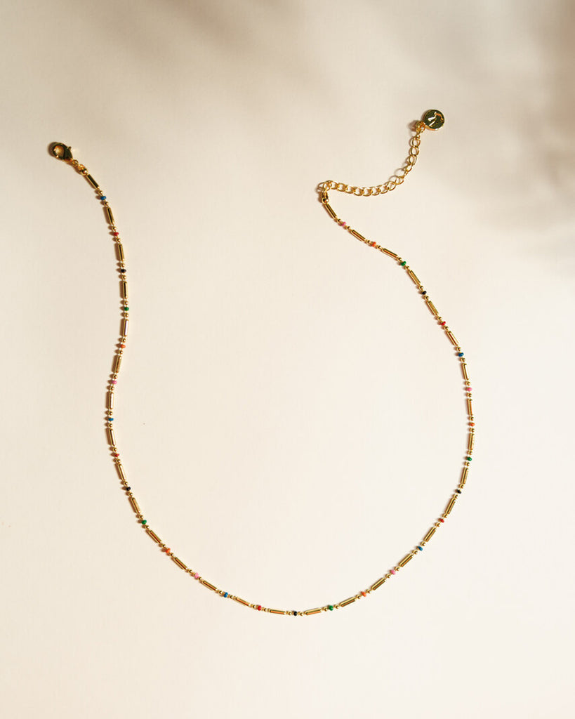 A gold chain necklace with small, dainty plastic beads throughout.