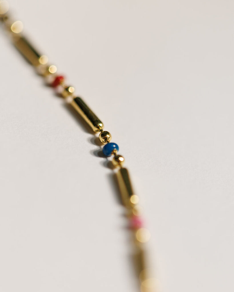 A gold chain necklace with small, dainty plastic beads throughout.