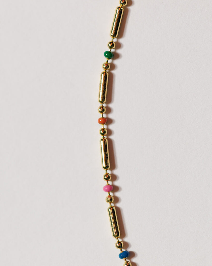 A gold chain necklace with small, dainty plastic beads throughout.