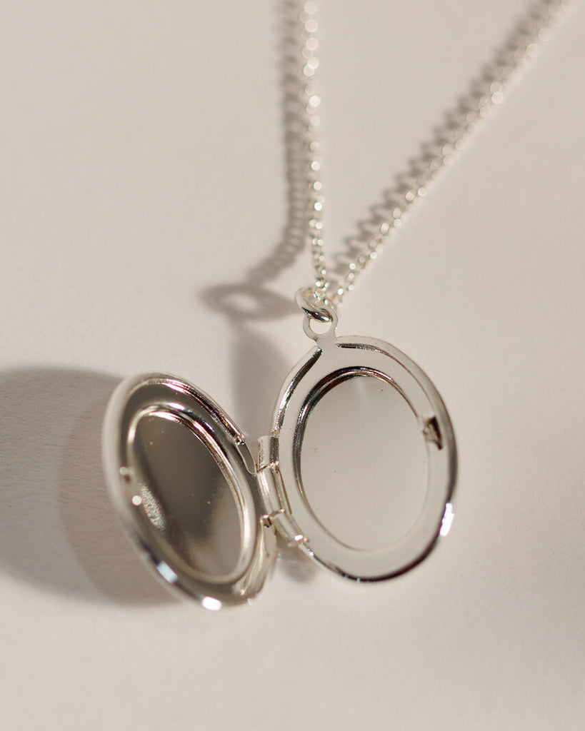 A silver necklace with an oval silver locket attached.