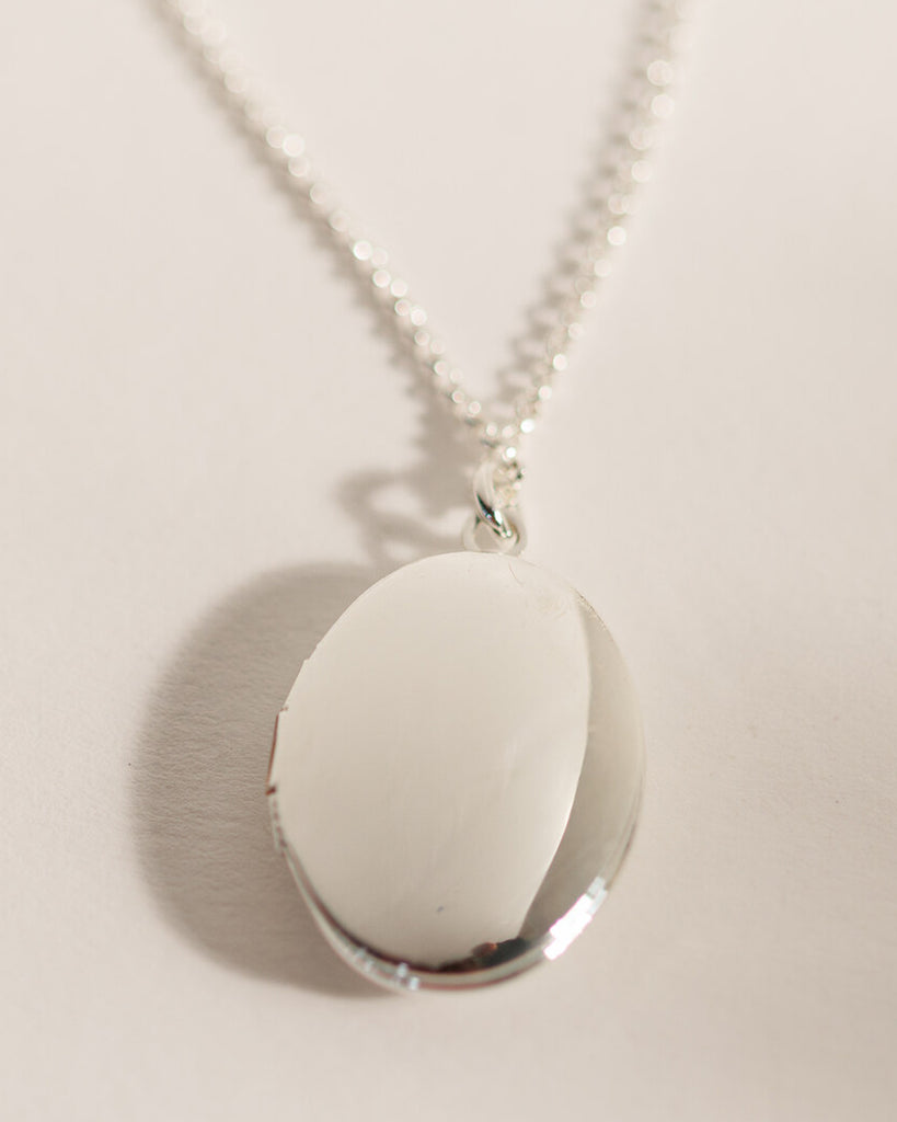 A silver necklace with an oval silver locket attached.