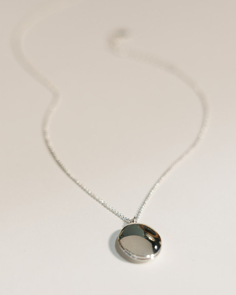 A silver necklace with an oval silver locket attached.