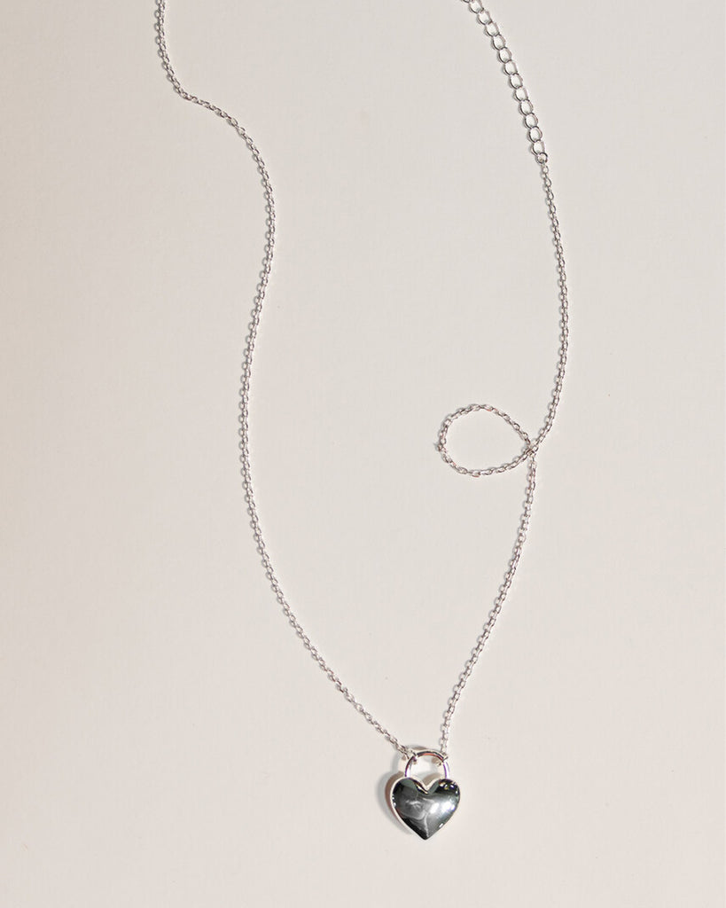 A silver necklace with a large silver heart charm.