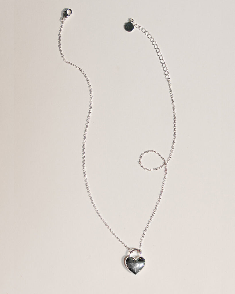 A silver necklace with a large silver heart charm.