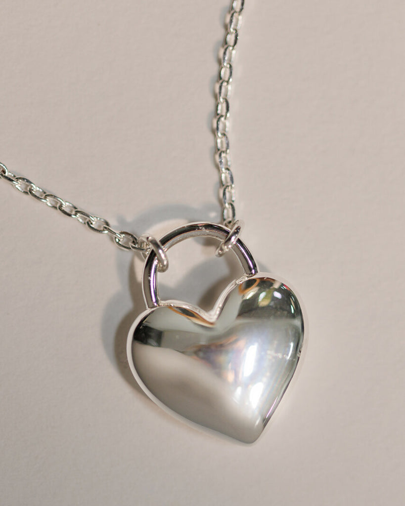 A silver necklace with a large silver heart charm.