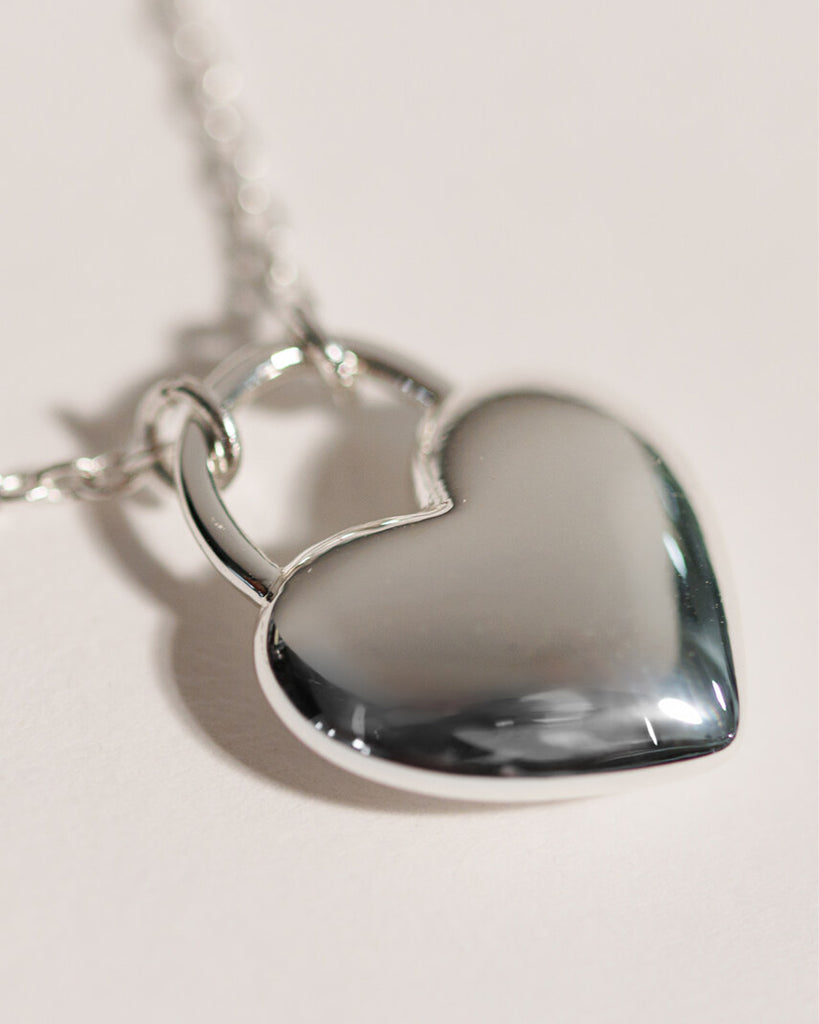 A silver necklace with a large silver heart charm.