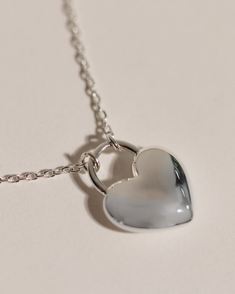 A silver necklace with a large silver heart charm.