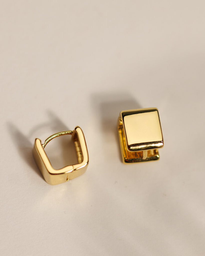 A pair of gold square huggie hoop earrings.