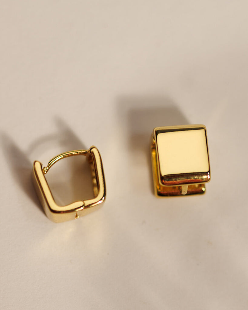 A pair of gold square huggie hoop earrings.