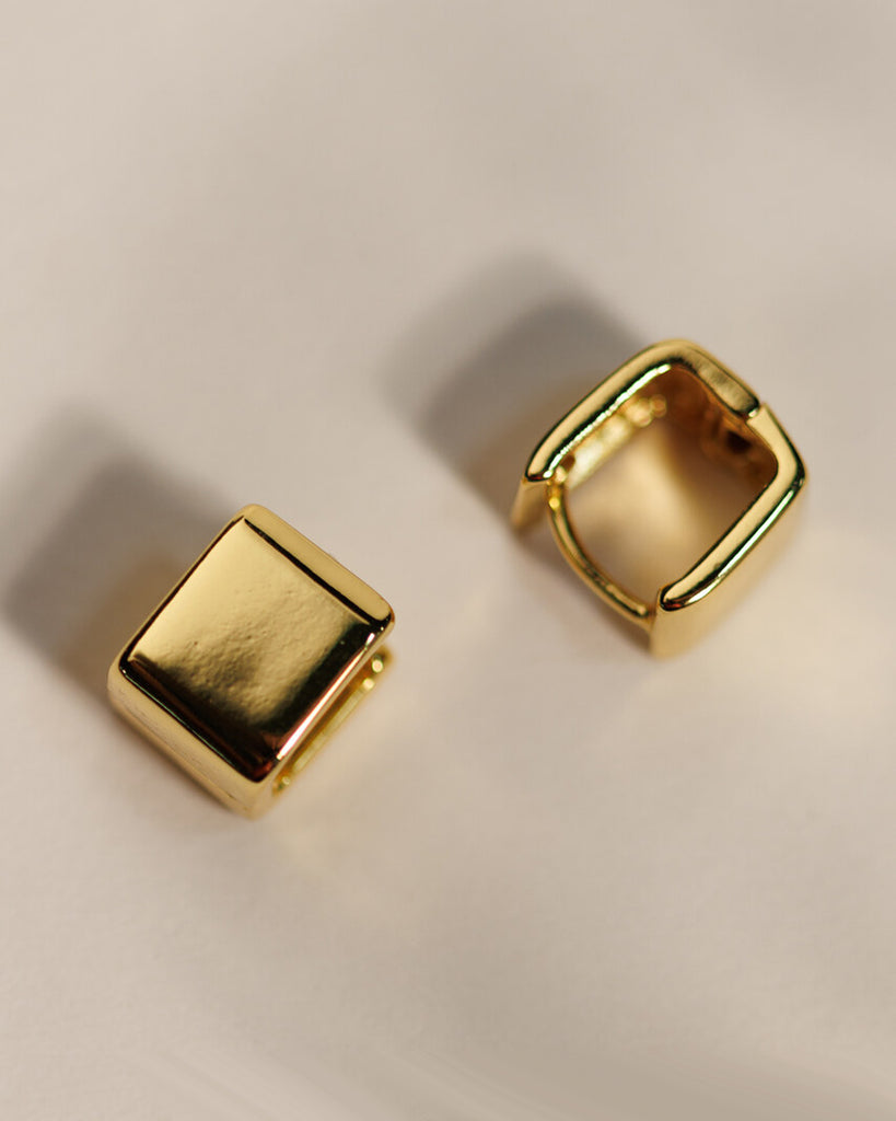 A pair of gold square huggie hoop earrings.