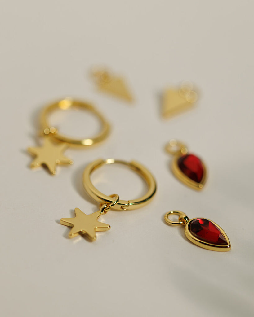 A set of small gold hoops with triangle, star and red gemstone teardrop charms.