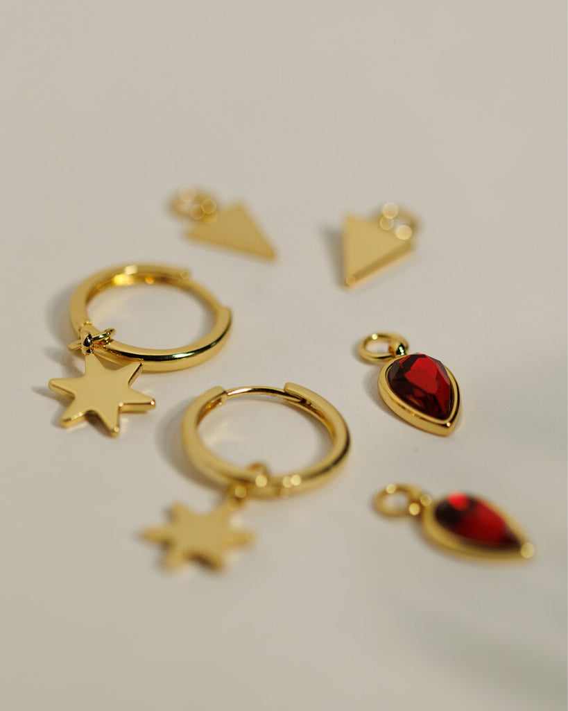 A set of small gold hoops with triangle, star and red gemstone teardrop charms.