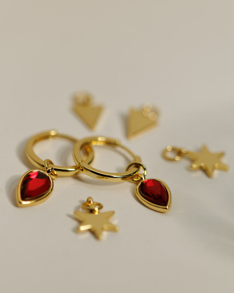 A set of small gold hoops with triangle, star and red gemstone teardrop charms.