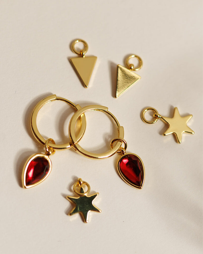 A set of small gold hoops with triangle, star and red gemstone teardrop charms.