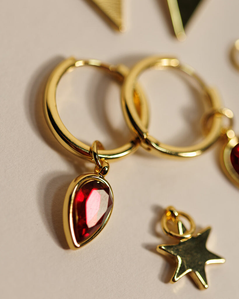 A set of small gold hoops with triangle, star and red gemstone teardrop charms.