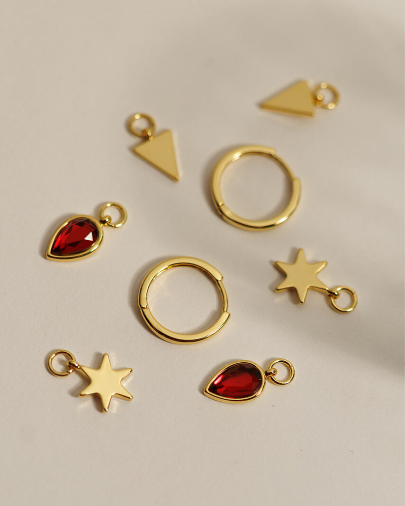 A set of small gold hoops with triangle, star and red gemstone teardrop charms.