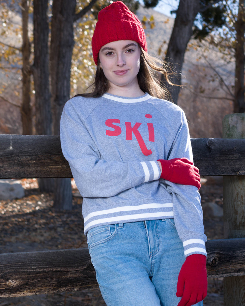 Woman in a grey pullover sweater with "ski" across the front in red lettering