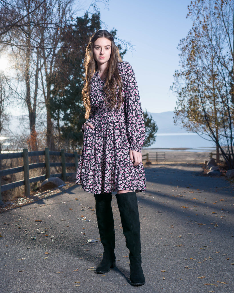 Woman in a black with pink floral print dress that has long sleeves and is knee-length