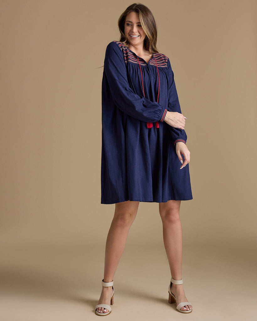 Woman in a long sleeve, knee-length, navy dress with red tassels