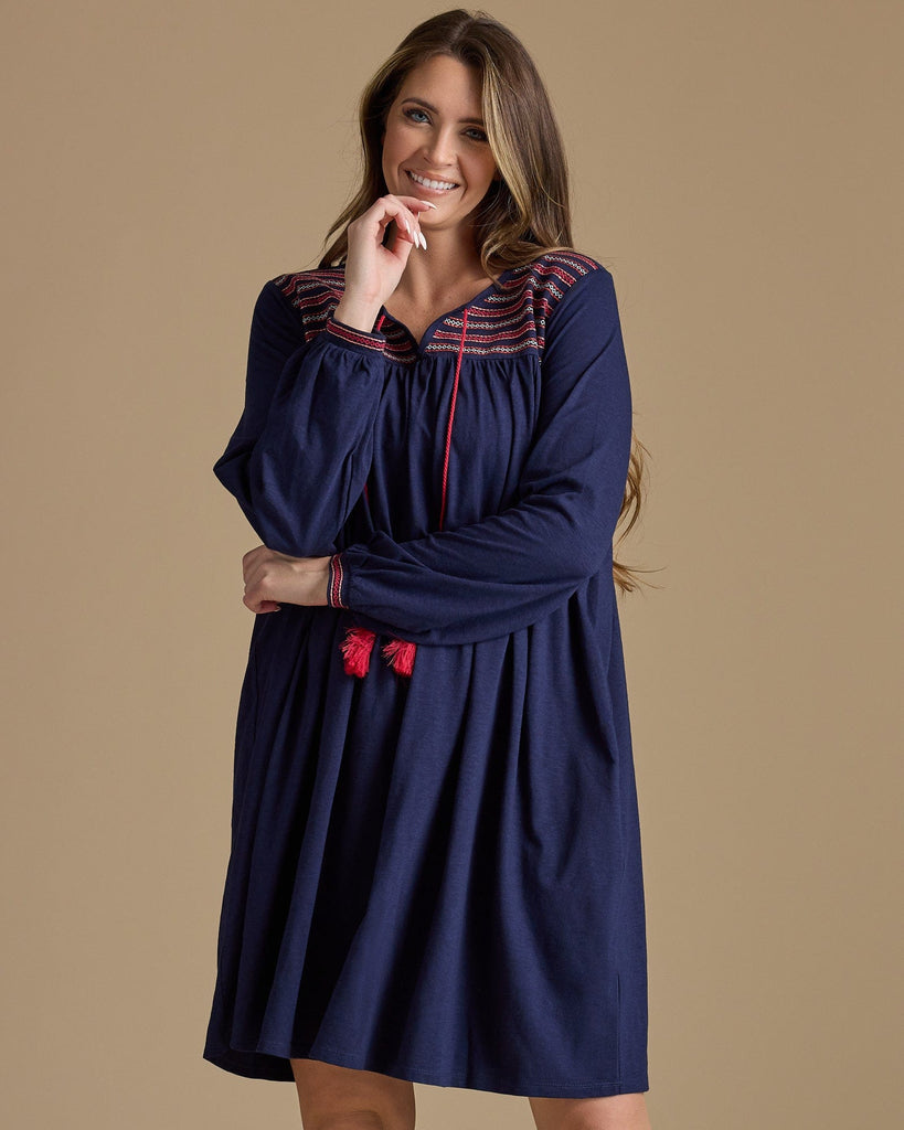 Woman in a long sleeve, knee-length, navy dress with red tassels