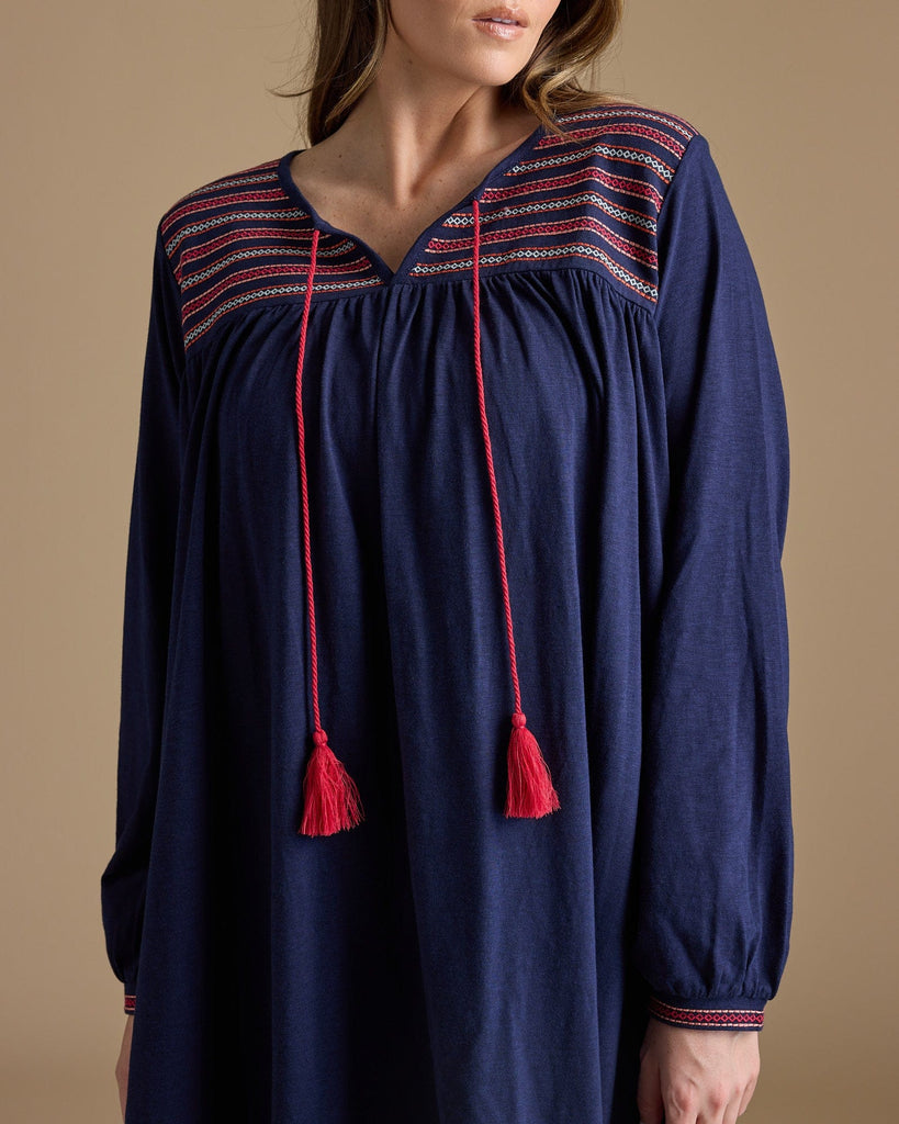 Woman in a long sleeve, knee-length, navy dress with red tassels