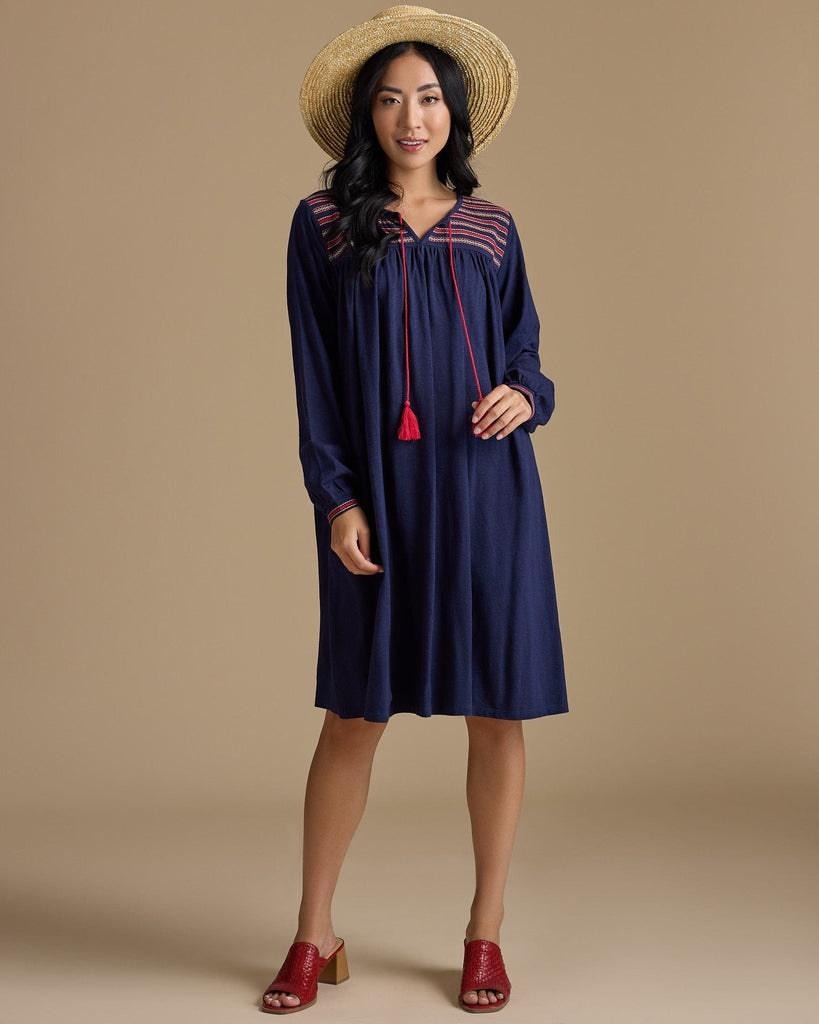 Woman in a long sleeve, knee-length, navy dress with red tassels