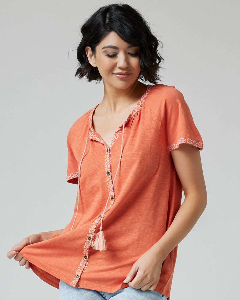 Woman in an orange top with short sleeves and buttons down the front