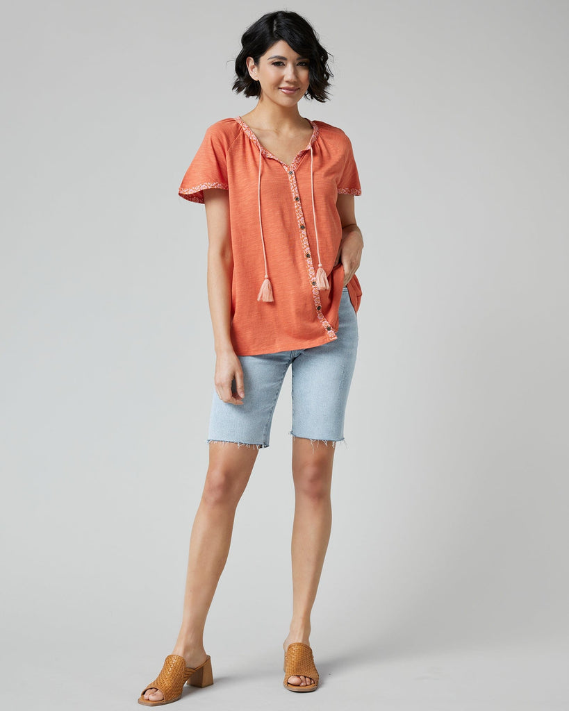 Woman in an orange top with short sleeves and buttons down the front