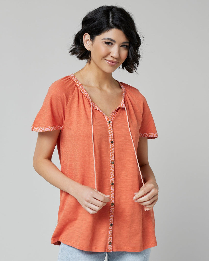 Woman in an orange top with short sleeves and buttons down the front