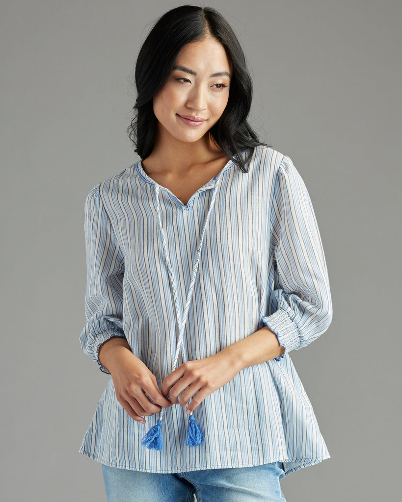 Woman in a blue blouse with 3/4 length sleeves, vertical stripes and tassels