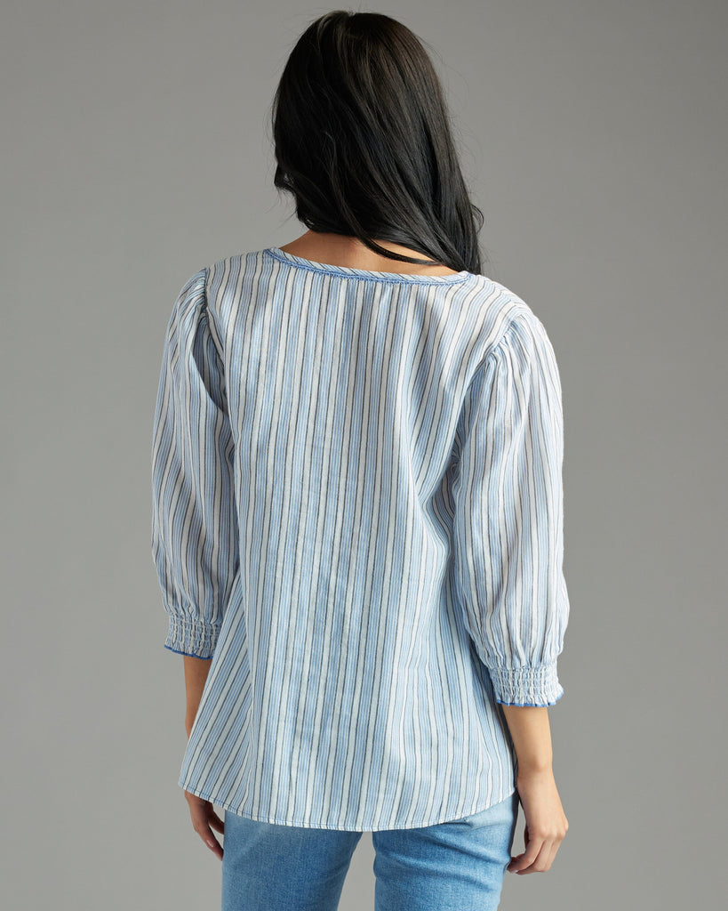 Woman in a blue blouse with 3/4 length sleeves, vertical stripes and tassels