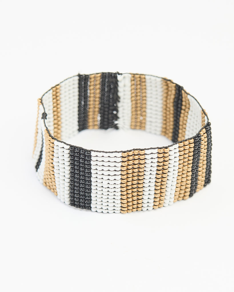 A wide beaded bracelet that stretches over the hand where the beads make a stripe pattern in black, white and gold colors.