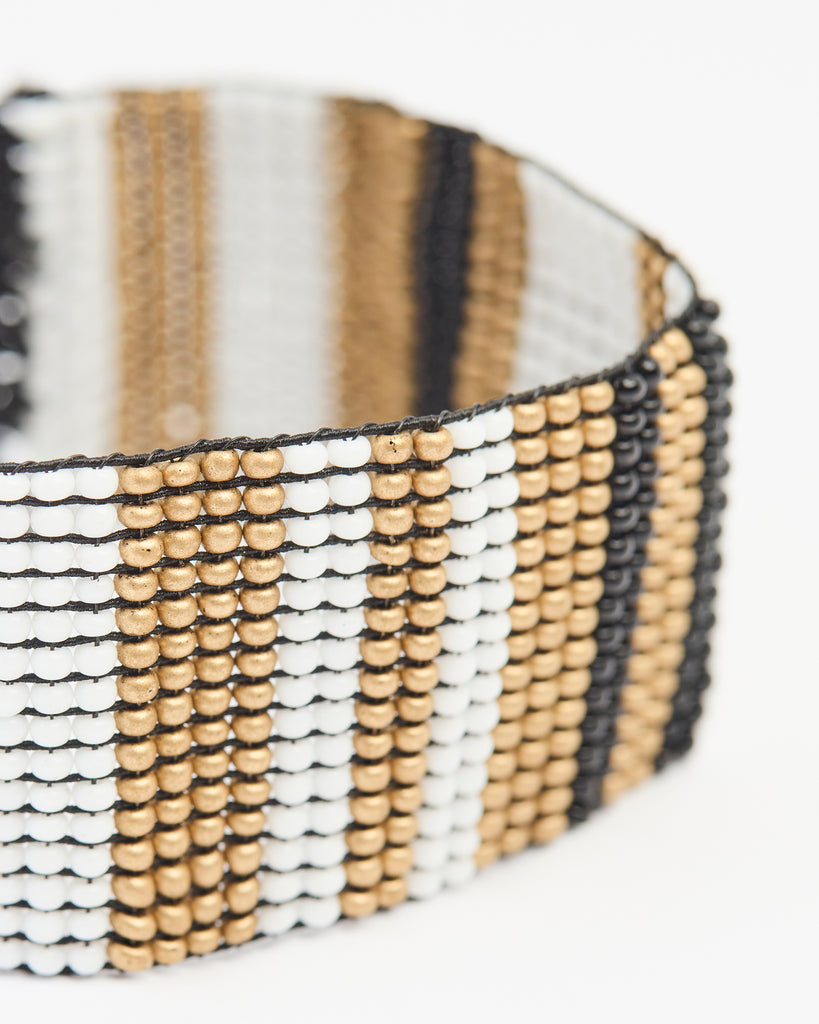 A wide beaded bracelet that stretches over the hand where the beads make a stripe pattern in black, white and gold colors.