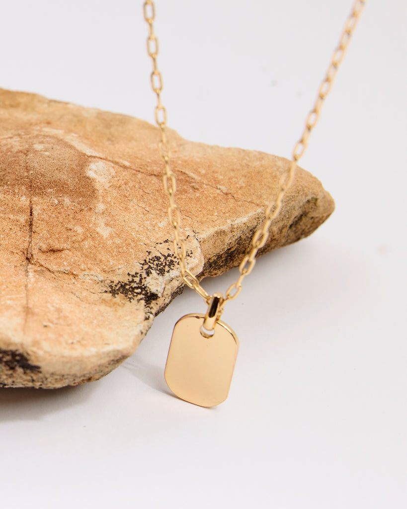 A gold necklace with a rectangular pendant attached.