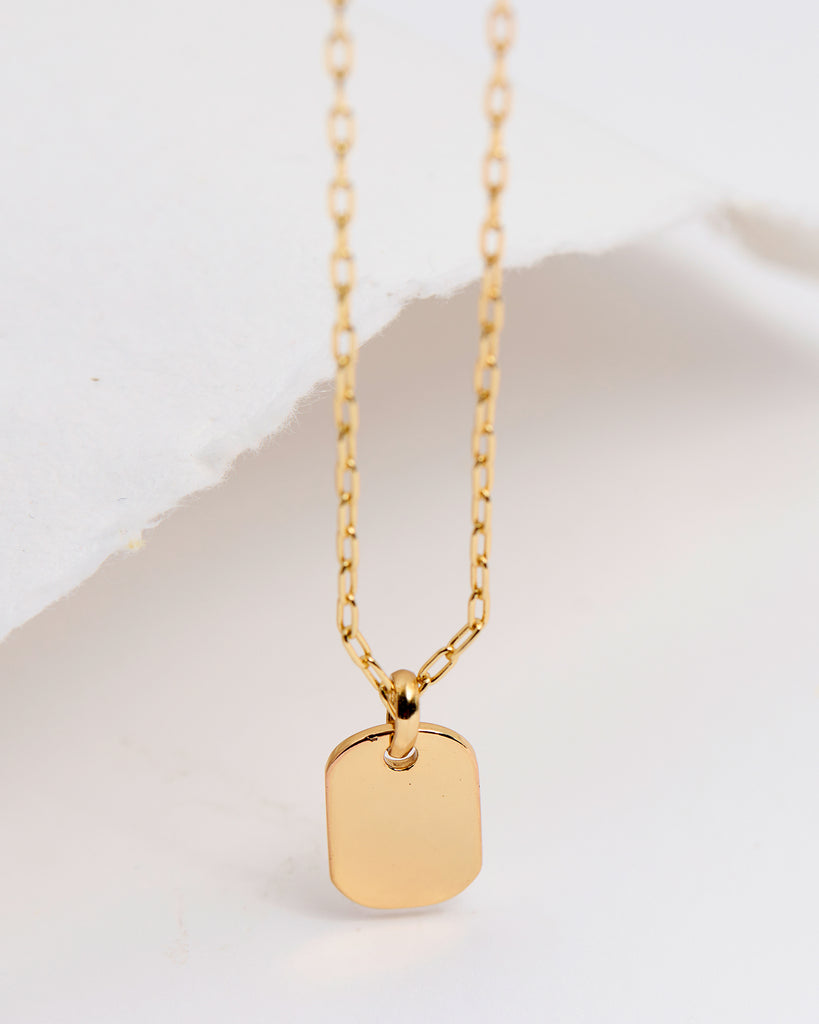 A gold necklace with a rectangular pendant attached.