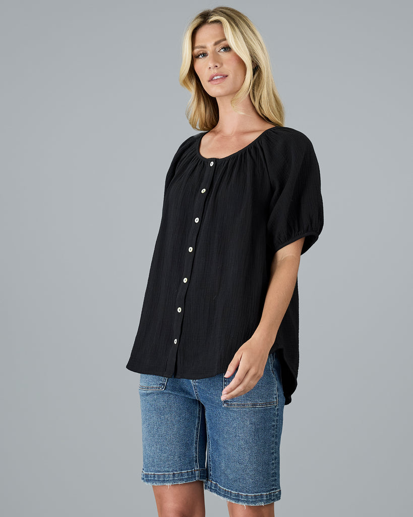 Model wearing a black, short sleeve, scoop neck blouse with white buttons down the front.