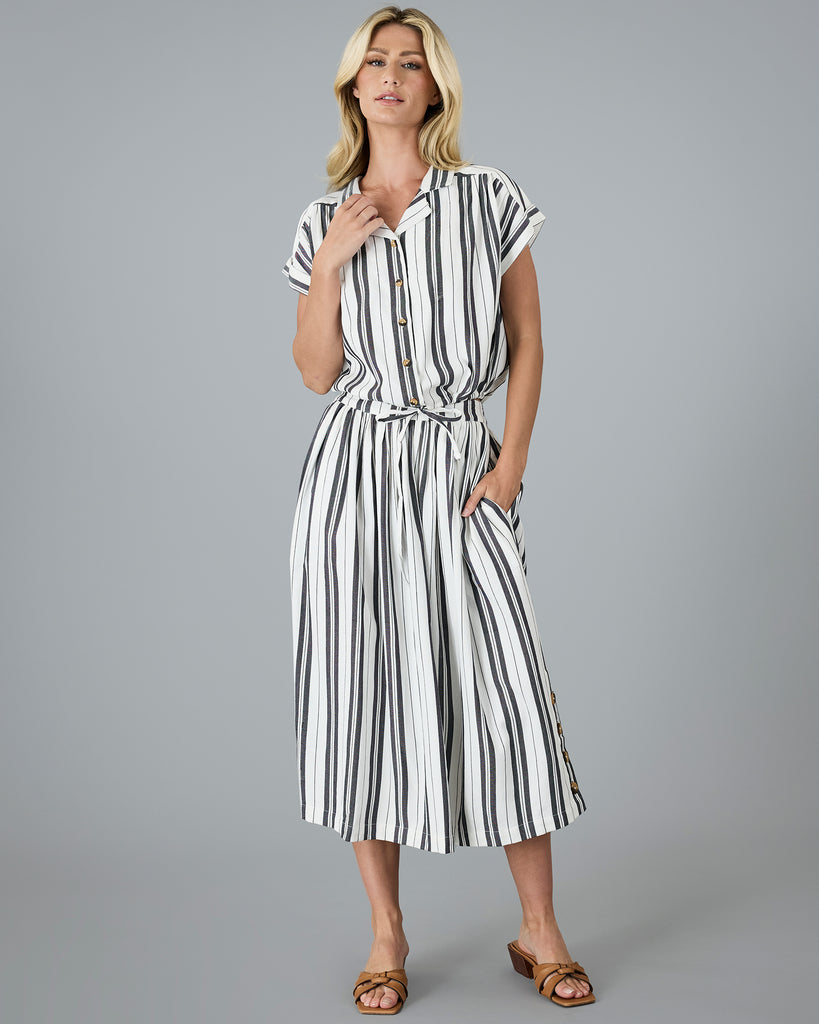 Model wearing a black and white vertical striped, short sleeved, collared, button-up blouse.