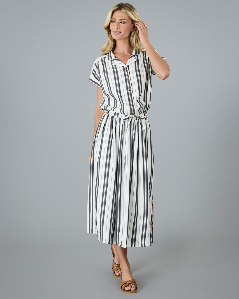 Model wearing a black and white vertical striped, short sleeved, collared, button-up blouse.