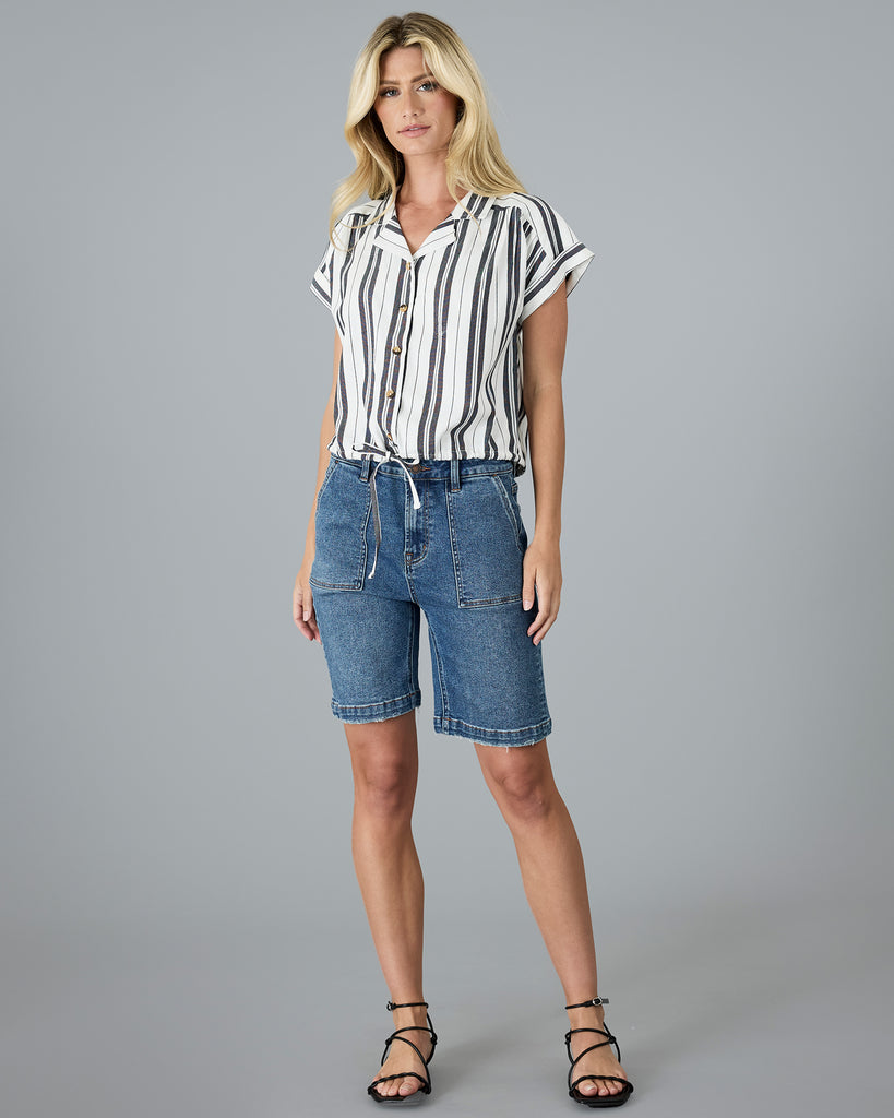 Model wearing a black and white vertical striped, short sleeved, collared, button-up blouse.