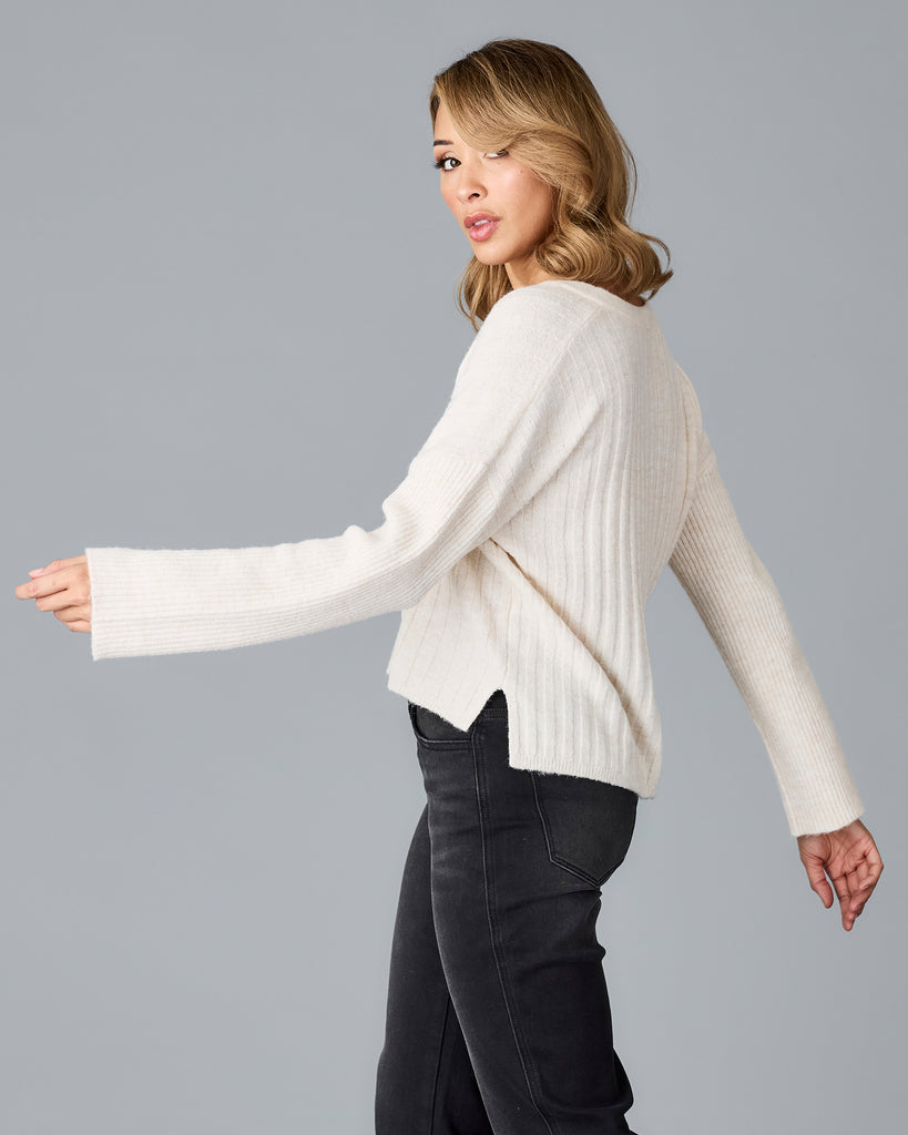 Model wearing a white long sleeve, v-neck, ribbed sweater