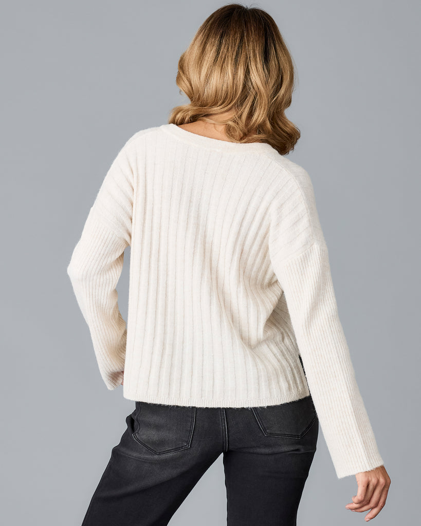 Model wearing a white long sleeve, v-neck, ribbed sweater