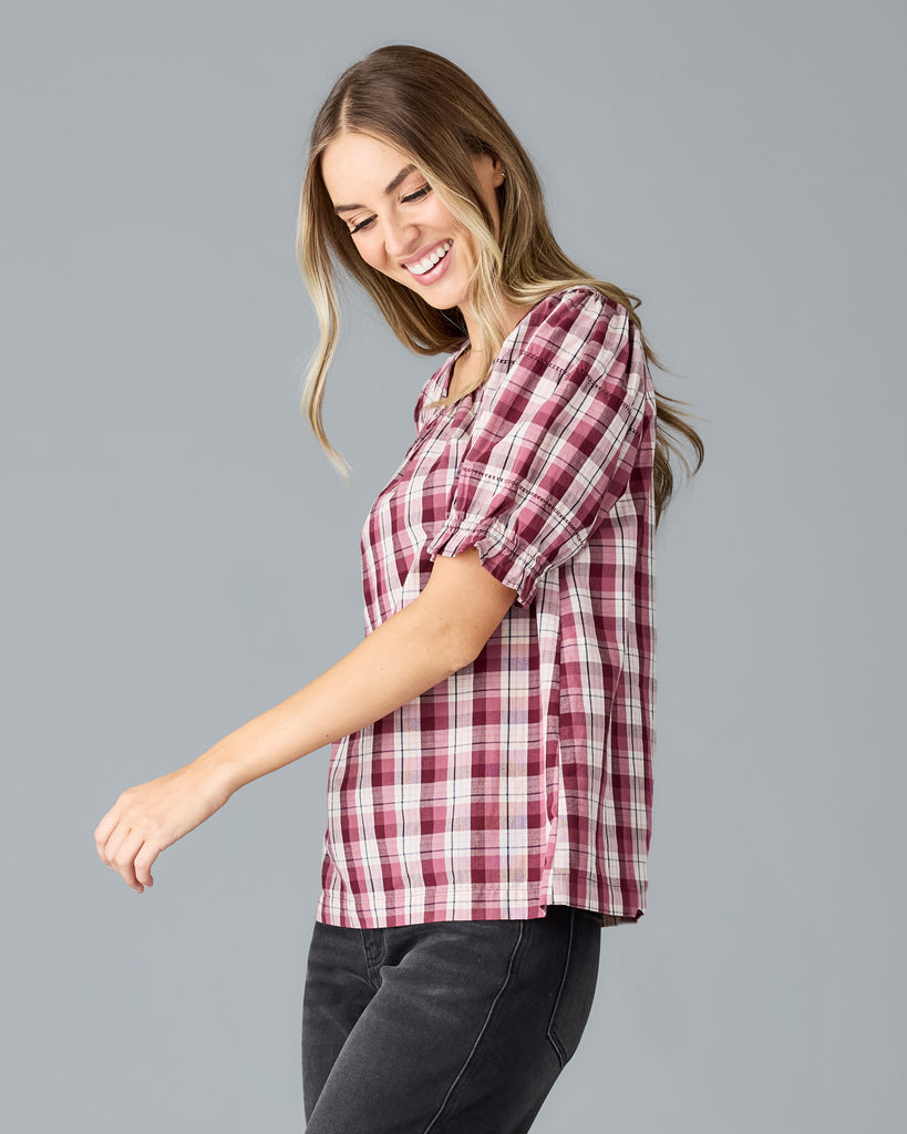 Model wearing a red and white plaid short sleeve, scoop neck blouse.