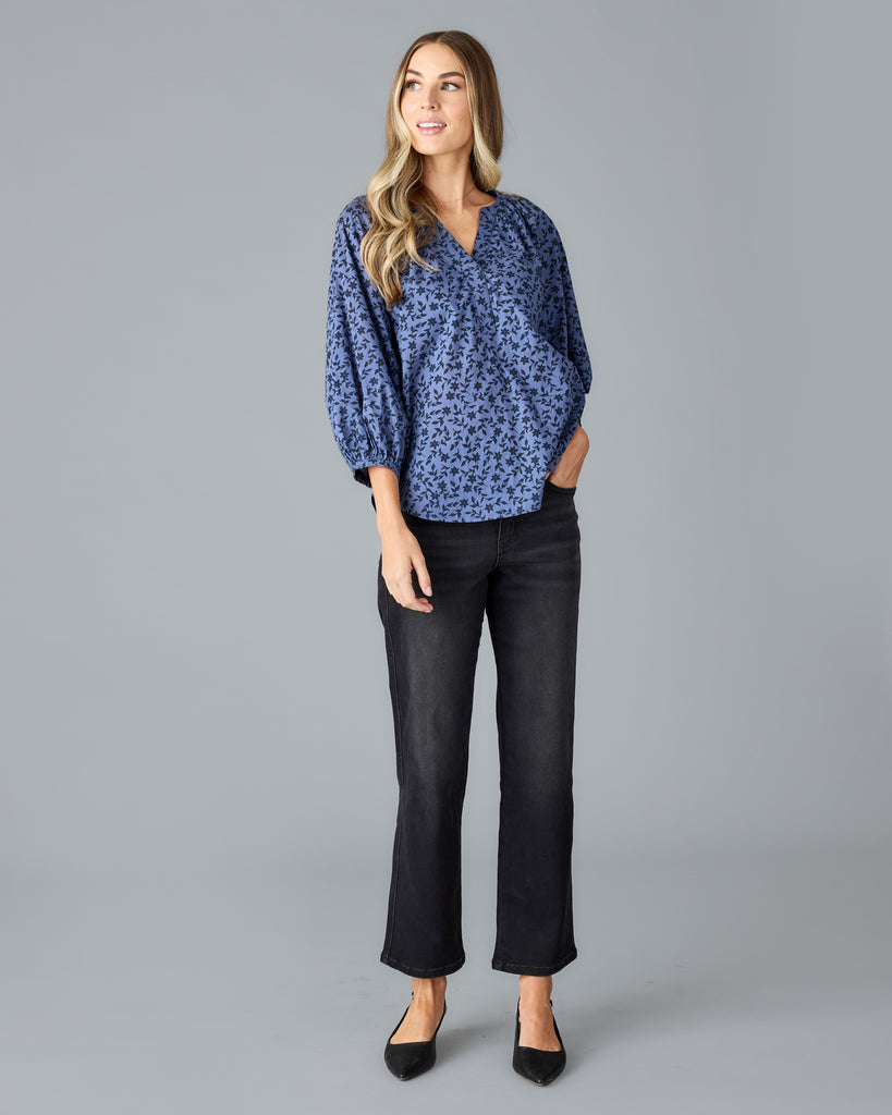 Model wearing a blue with black floral print long sleeve, v-neck, look fitting blouse.