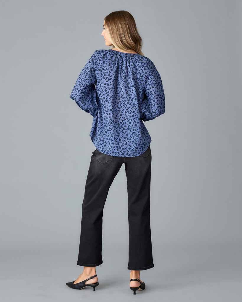 Model wearing a blue with black floral print long sleeve, v-neck, look fitting blouse.