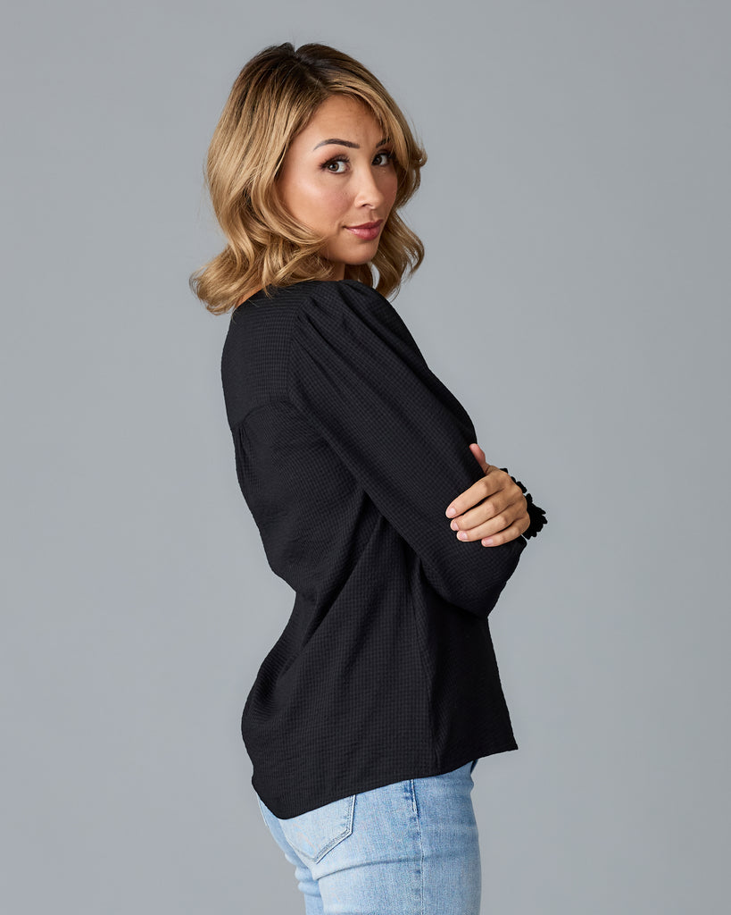 Model wearing a black long sleeve, v-neck loose fitting blouse.