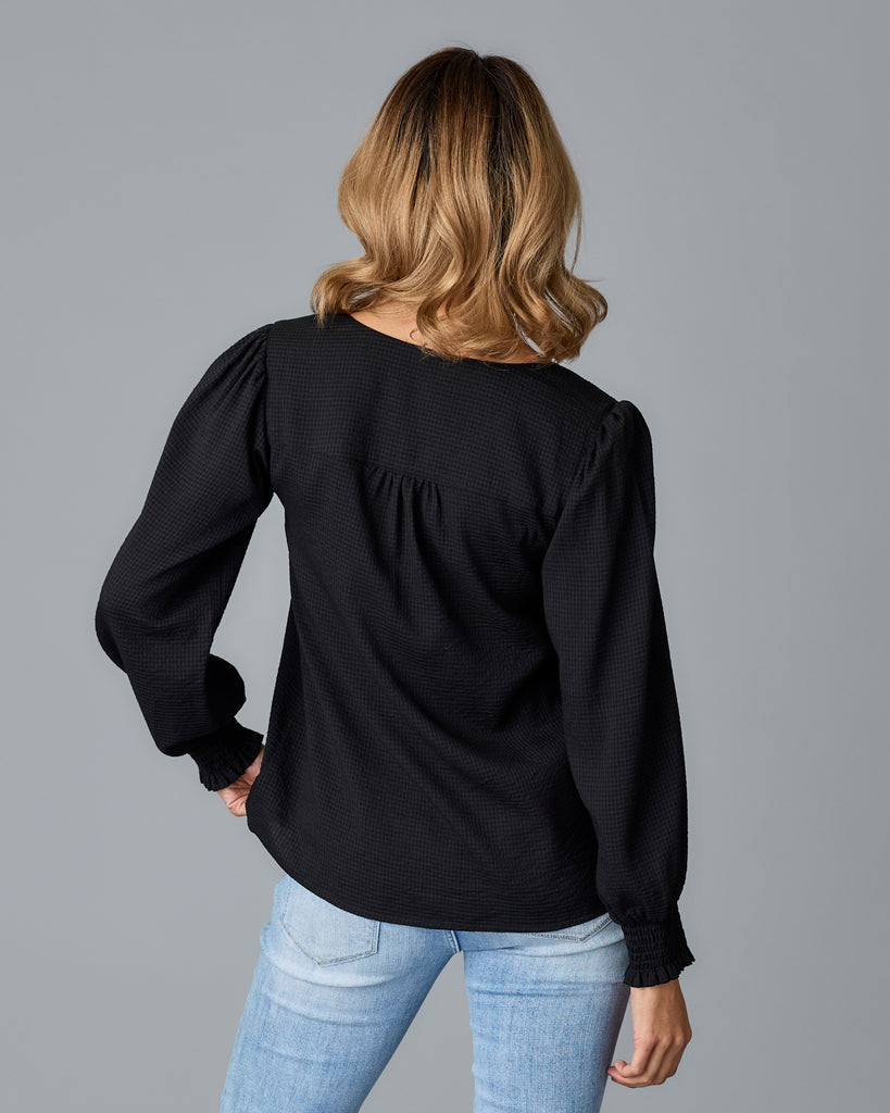 Model wearing a black long sleeve, v-neck loose fitting blouse.