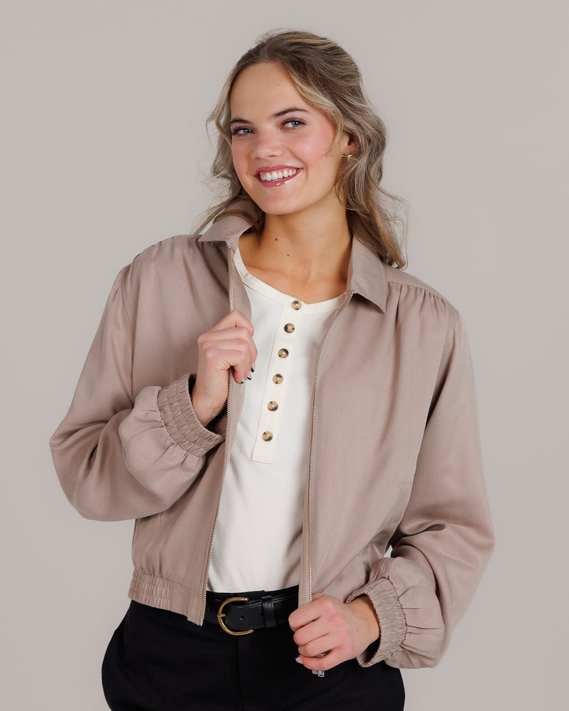 Model wearing a tan long sleeve, collared, lightweight jacket.