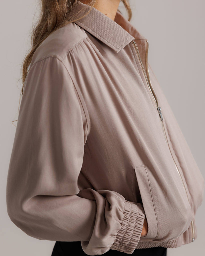 Model wearing a tan long sleeve, collared, lightweight jacket.