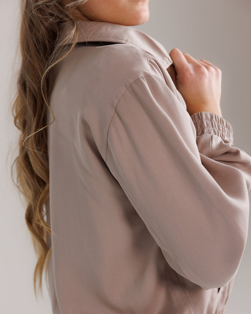 Model wearing a tan long sleeve, collared, lightweight jacket.