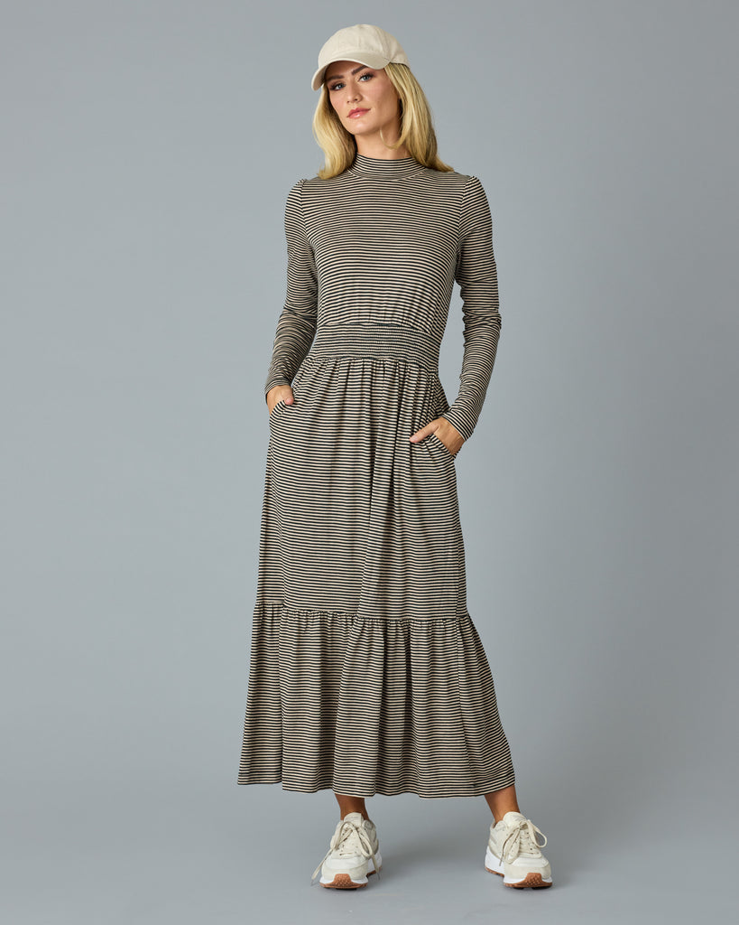 Woman in a black and tan thin striped maxi dress with long sleeves, a mock neck and pockets